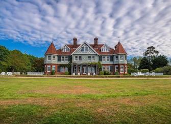 A grand Victorian Manor House with two turreted wings overlooks a large lawn.