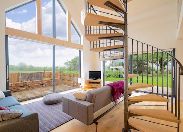 Lounge with large glass gable end window, sofas and spiral staircase.