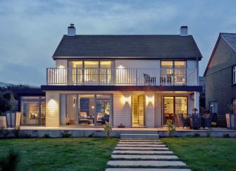 A modern 2-storey house with a full length balcony with all lights on in the dusk.