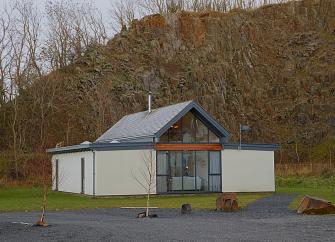 A contemporary Northumberland holiday lodge beneath a sheer rocky hill face.