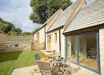 A side elevation of a luxury Cotswold Barn conversion with wide, full-height sliding French Windows.