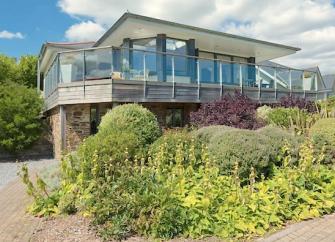 A contemporary wood and glass bungalow with a wrap-around deck overlooks a shrub-filled garden.