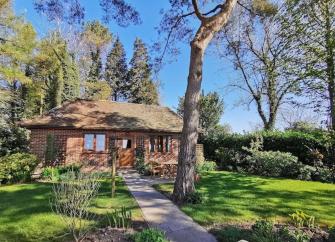 The exterior of a brick-built Dorset bungalow is surrounded by lawns, shrubs, and mature trees.