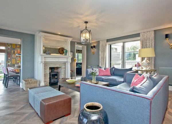 A large and luxuriously-furnished lounge with a French window, wood-burner and arch to a kitchen.