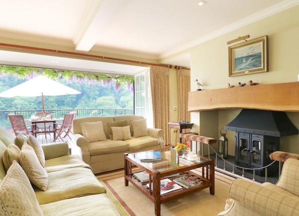 A lounge withbiig sofas, coffee table, wood burner and open bifold doors to a waterside terrace.