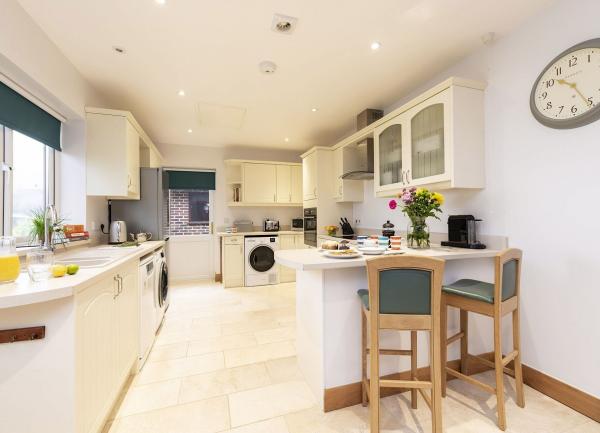 A large immaculate modern kitchen with integrated white goods and breakfast bar with stool.