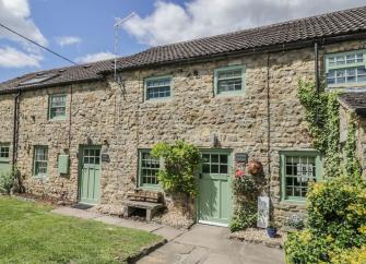 A terrace of 3-stone-built Bedale holiday cottages facing a lawn.
