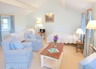 A tall stone barn conversion and annexe surrounded by a lawn, open fields and mature woods.