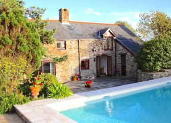 An outdoor swimming pool overlooked by a stone-built holiday cottage in North Devon