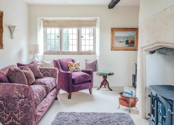 A Cotswold cottage lounge with a sofa, armchair and wood-burner.