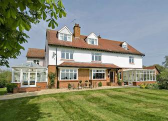 Exterior of a large country house with a conservatory and large lawn.