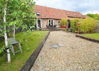 A shingle path leads up to a stone-built Norfolk bungalow with two long lawns.