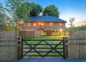 A timber house on stilts beneath lime trees overlooks a large fenced garden.