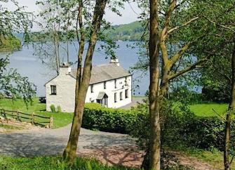 Exterior of a large 2-story house surrounded by a lawn on the shores of a large lake.