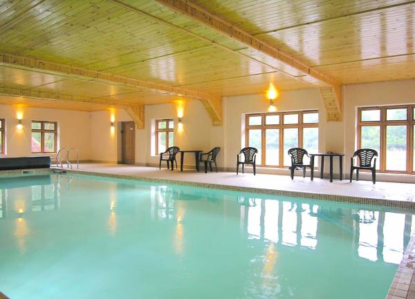 A large indoor heated swimming pool with chairs on the pool terrace.