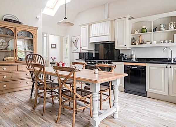 A kitchen with oak floorboards, fitted units including a washing machine, twin cooker, a pine breakfast table and a dresser with glass doors.