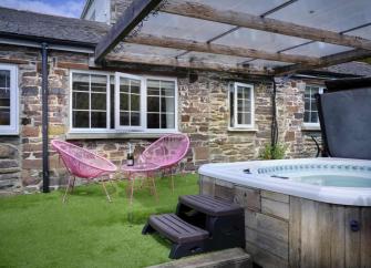 A stone built Exmoor cottage faces a lawn containing a sheltered hot tub and a two outdoor chairs around a tea-table.