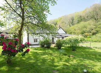 Exterior of a North Devon mill cottage surrounded by gardens in a valley floor.