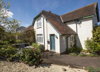 The exterior of a detached Somerset holiday cottage and shrub-filled garden.