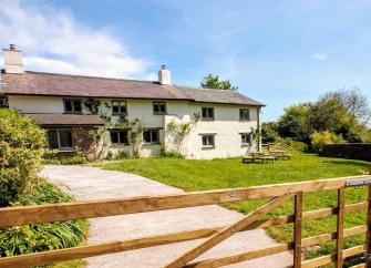Large Exmoor holiday cottage overlooks a spacious lawn and a drive with a wooden 5-bar entry gate.