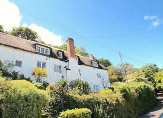 A 3-storey Somerset longhouse overlooks a steep-banked country lane.