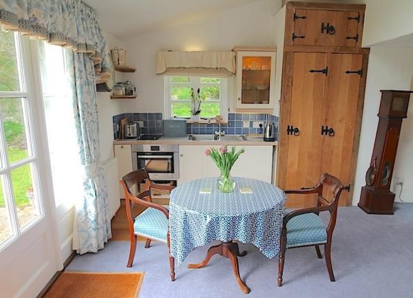 A dining table for two and compact kitchenette with an oven, fridge and French windows to a riverside garden.