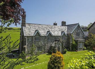 A large stone-built Exmoor cottage surrounded by trees and open fields.