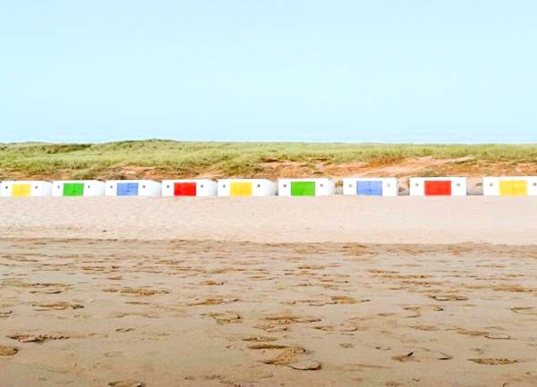 Multi-coloured beach huts nestle on the sand beneath sand dunes ion Woolacombe Beach..