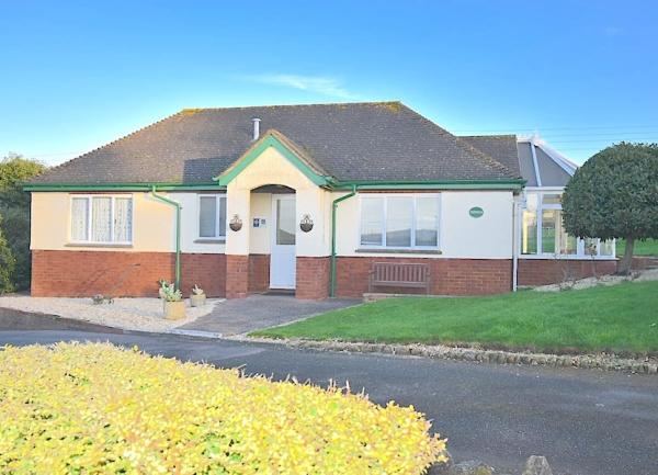 Front exterior of a holiday bungalow with a  facing a lawn and an off-road parking space. porch