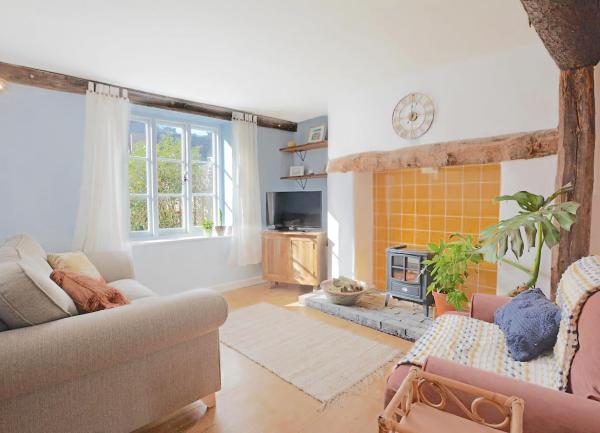 A cottage lounge with oak beams, an armchair, sofa, electric wood burner, TV and coffee table.