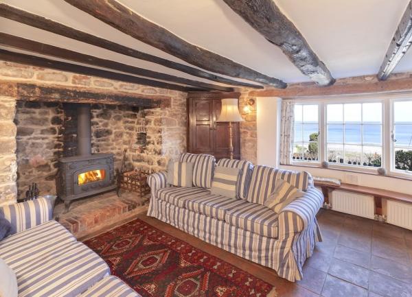 A lounge with an inglenook fireplace enclosing a wood-burner and windows offering sea views over Porlock Bay.