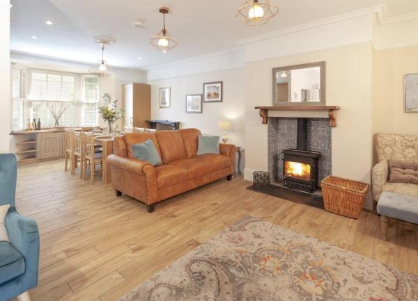 Pine-floored lounge with a wood-burner containing a sofa, easy chairs beyond which is a dining area with table and chairs 
