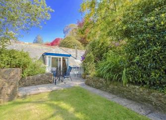   A footpath between a lawn and mature shrubs leads to a stone-built rural cottage.