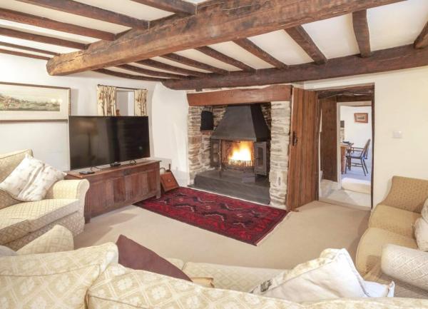 A country cottage lounge with beamed ceilings, an inglenook with a wood-burner and a semi circle of sofas facing a TV.