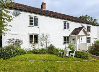 A Somerset farmhouse overlooks a large lawn lined by shrubs.