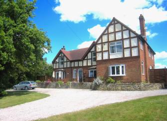 A modern cross-timbered gable overlooking a drive, lawn and a spacious parking area.