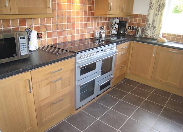 Kitchen corner with fitted floor and wall cupboards, twin oven, dishwasher and other kitchen appliances.