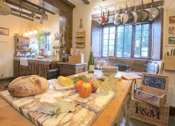An old-pinewood kitchen table bearing a marble cheeseboard and cheeses in a cottage kitchen.