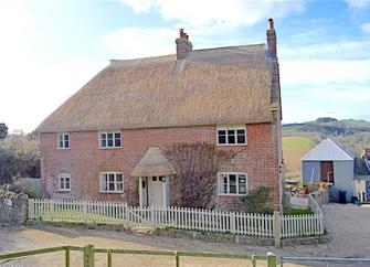 A Thatched farmhouse with a garden surrounded by a picket fence.