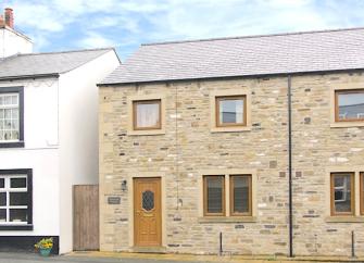 A stone-built, end of terrace cottage overlooking an empty street.