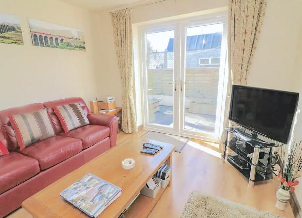 A wood-floored lounge with French windows containing a leather sofa, coffee table and TV.