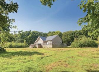 A single-storey eco-lodge surrounded by a deck and open fields.