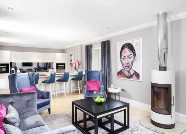 Luxuriously furnished loungewith a woodburner and sofas with a kitchen breakfast bar in the background.