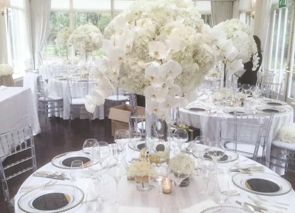 Tables laid for 7 with a large floral decoration in their centres.