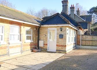 Exterior of a1930s brick built bungalow with a patio and shingled secure parking area.