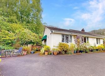 Exterior of a bubgalow surrounded a a garden with trees and mature shrubs and off-road parking space