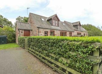 Exterior of a stone-built, semi-detached cottage with a  large, securely hedged-iin garden.