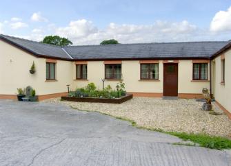 A single-storey barn conversion with right-angled wings faces a paved courtyard.