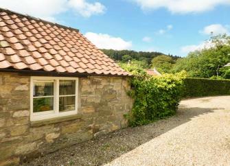 A semi-detached cottage with an enclosed front porch and a front garden behind a low stone wall
