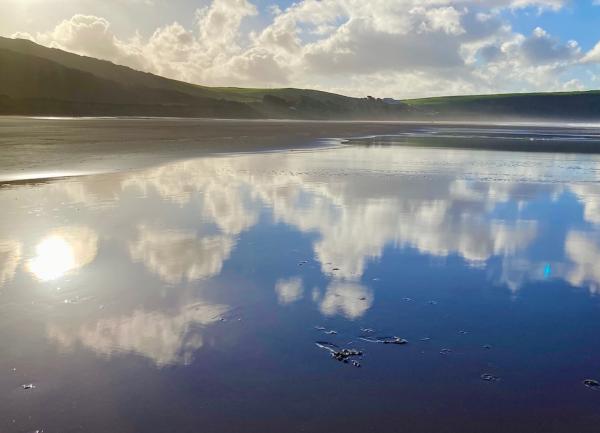 Clouds reflect in the wet sand of a winter beach.